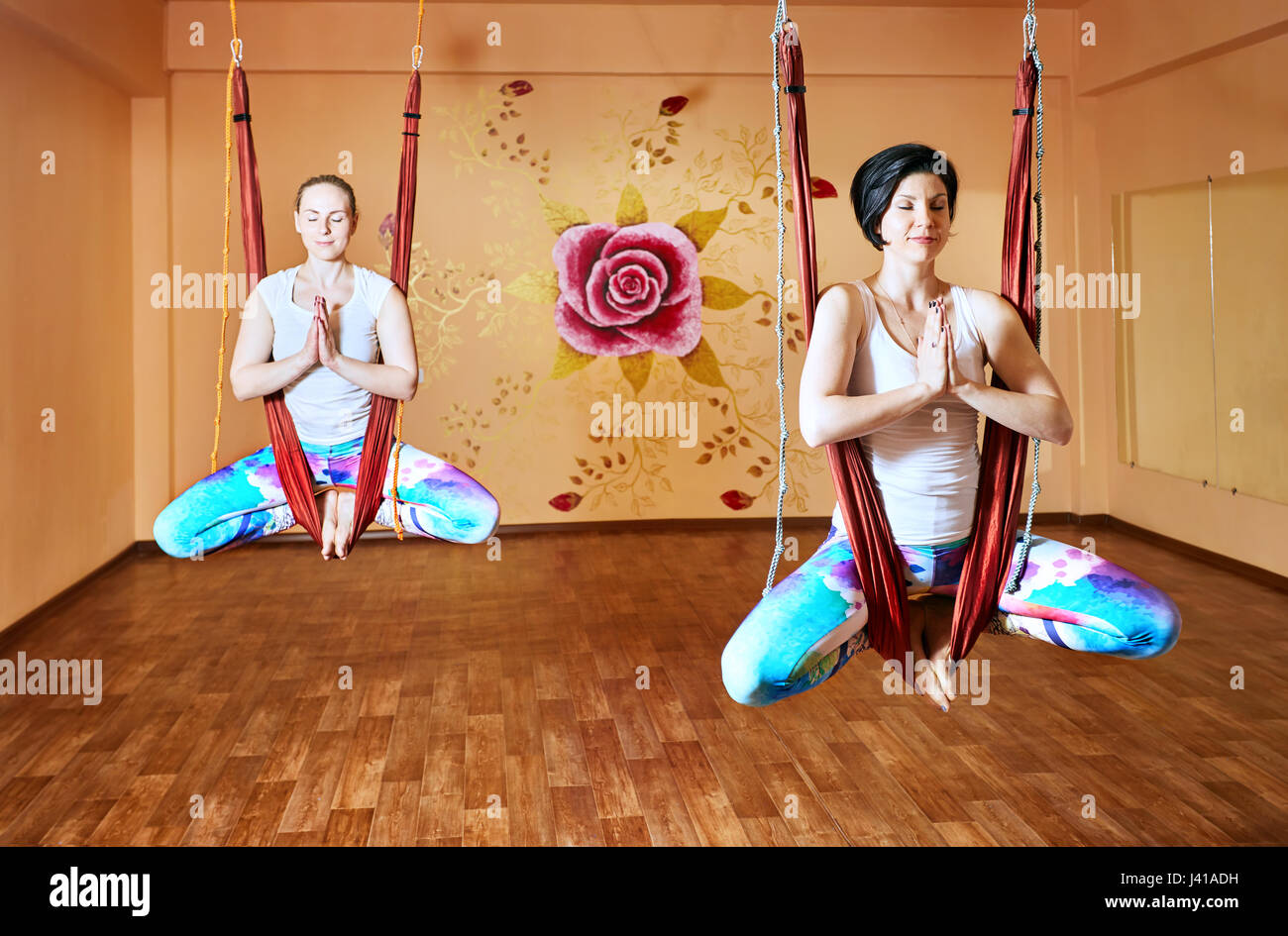 Zwei junge Frau beim Antigravity Yoga in Hängematte im Wellnessstudio mit Rose an der Wand Stockfoto