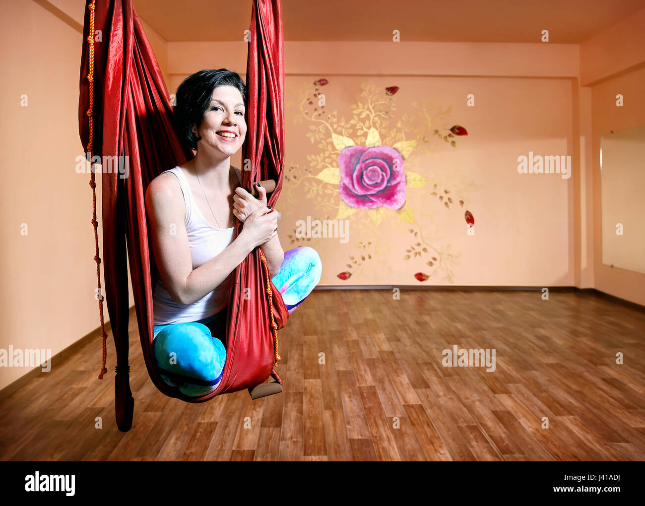 Junge Frau beim Antigravity Yoga in Hängematte im Wellnessstudio mit Rose an der Wand Stockfoto