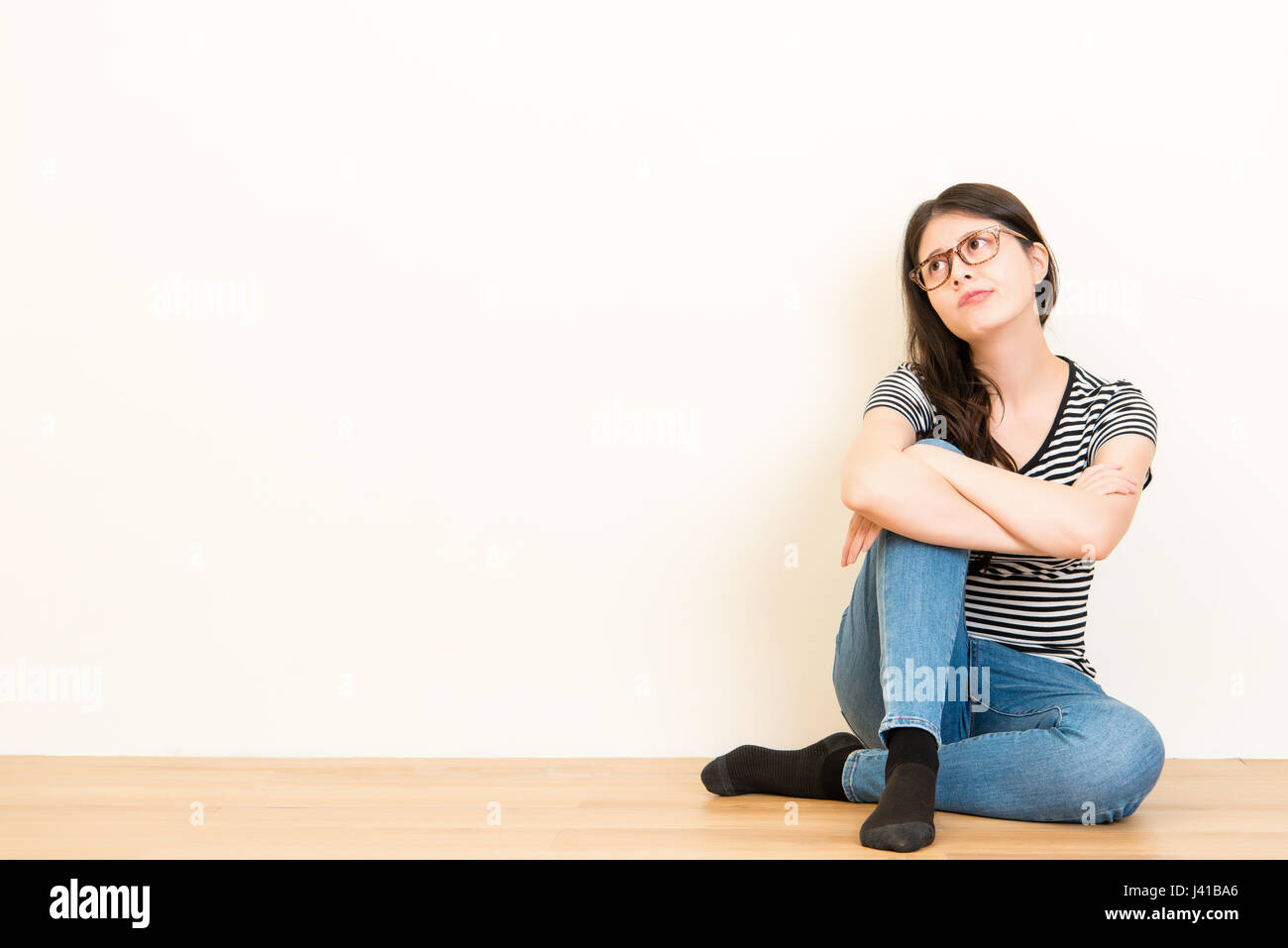 sehr schön verwirrt Student Frau denkt und träumt mit Freizeitkleidung auf Holzboden über leere Kopie Raum weiße Wand Hintergrund sitzt. Stockfoto