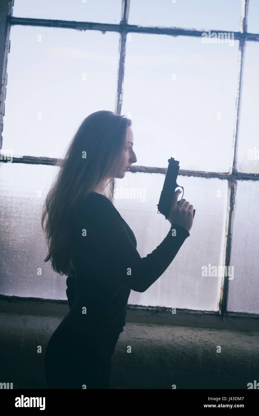 Seitenansicht einer Frau mit einer Pistole am Fenster Stockfoto