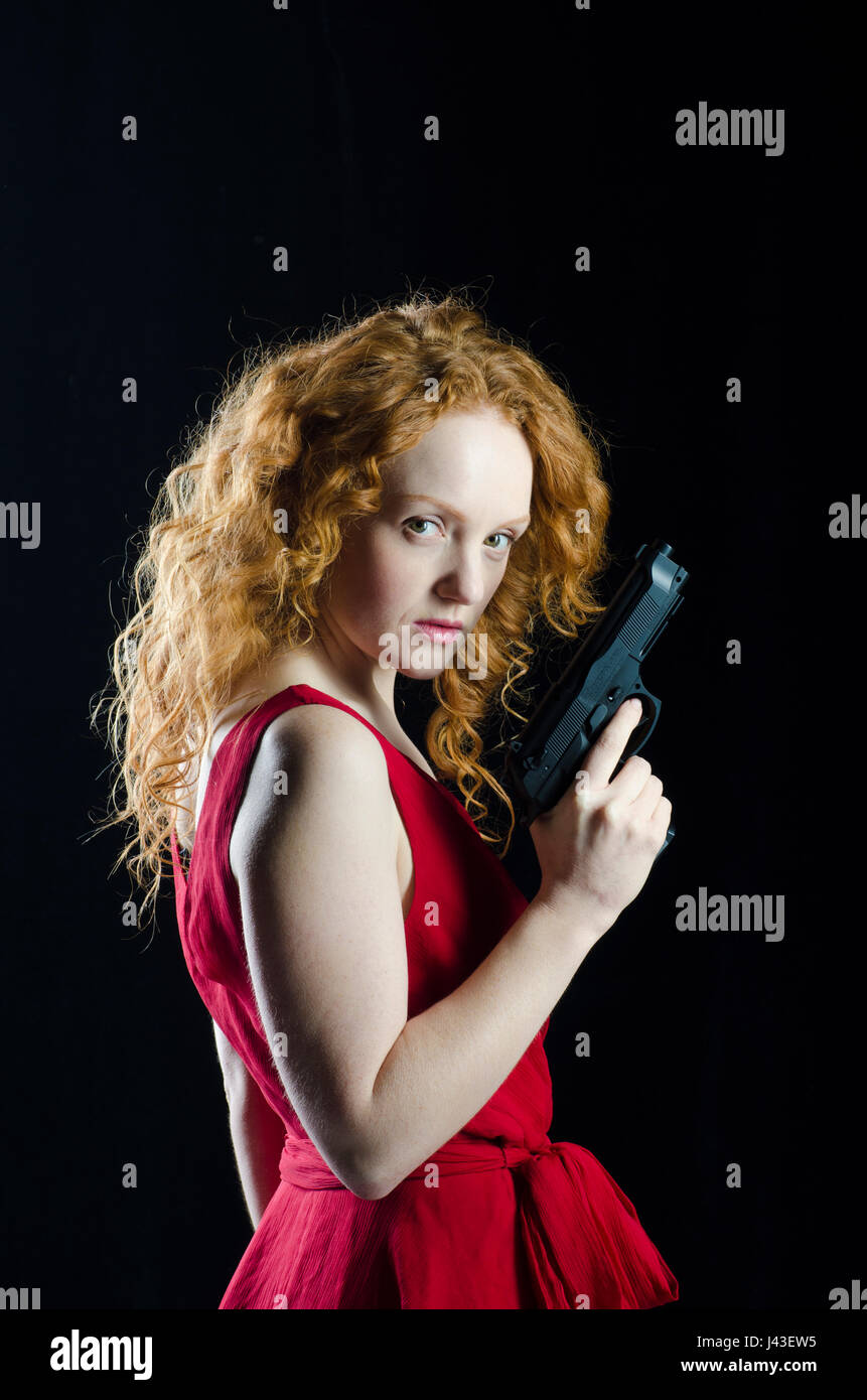 Schöne rothaarige Frau trägt ein rotes Kleid mit einer Pistole Stockfoto