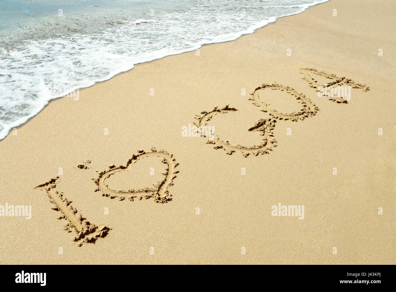 Weiche Welle des blauen Ozeans am Sandstrand mit Worten auf "Sand ich liebe Goa" Stockfoto