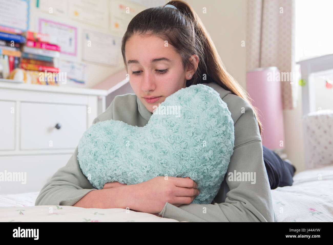 Junges Mädchen auf Bett umarmt Herz geformten Kissen liegend Stockfoto