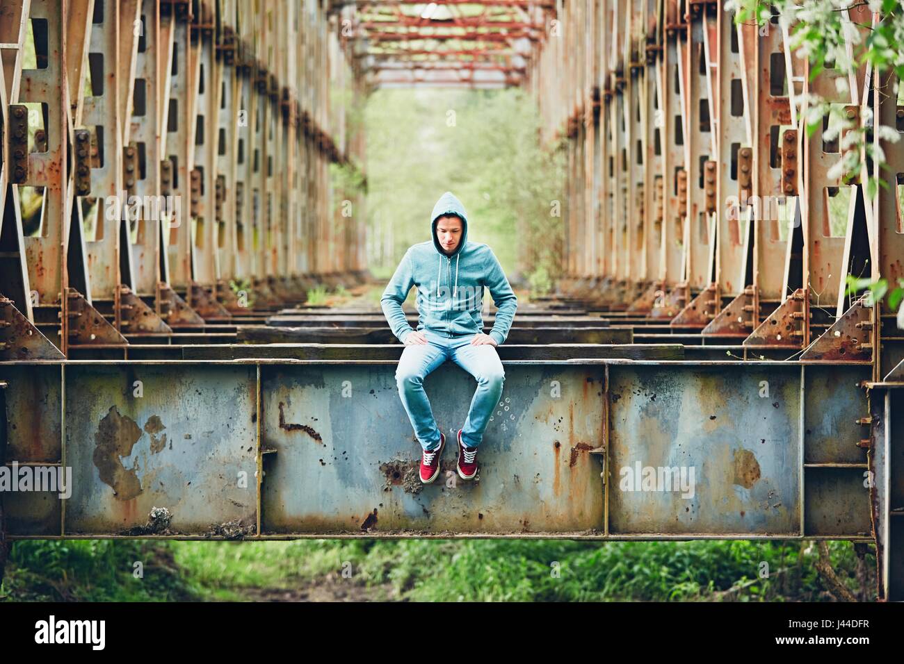 Trauriger Mann sitzt auf der verlassenen rostigen Brücke. Konzept für Traurigkeit, Einsamkeit und vieles mehr. Stockfoto