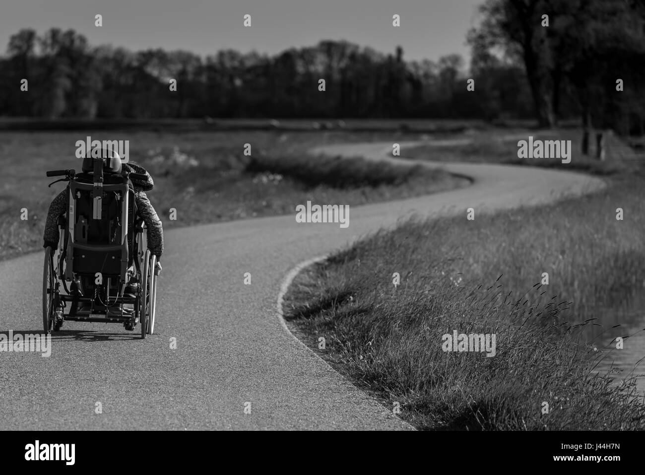 Eine behinderte Person in einem Rollstuhl alleine auf einer kurvenreichen Straße Stockfoto