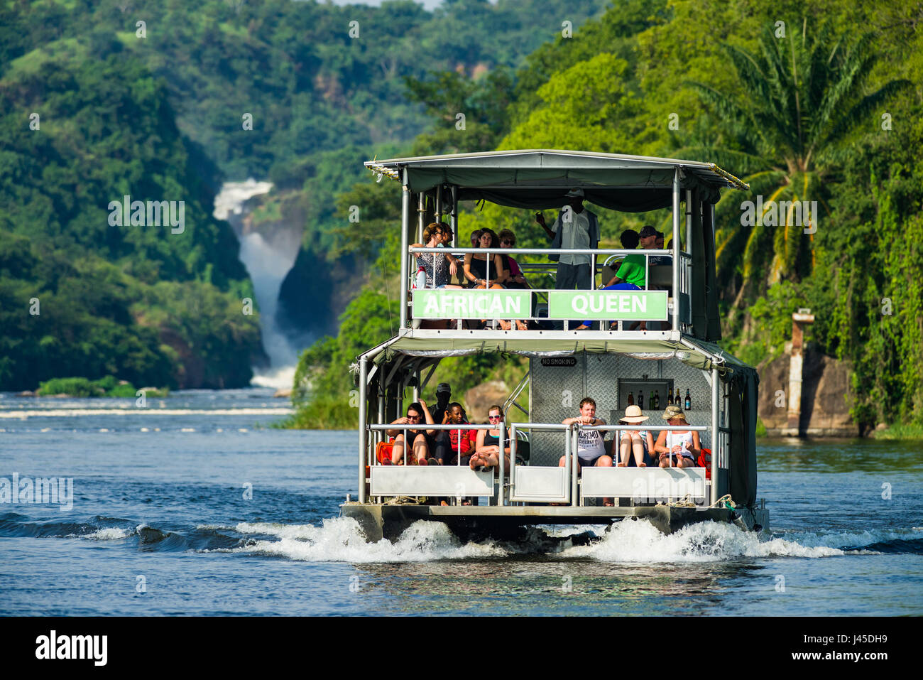 Tour Boot mit Touristen auf Victoria Nil mit Murchison Falls im Hintergrund, Uganda Stockfoto
