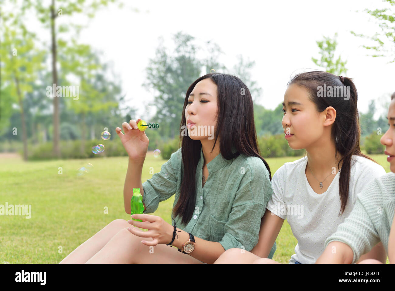 Schlag-Bläschen-Mädchen. Draußen sitzen auf einem Park-Rasen Stockfoto