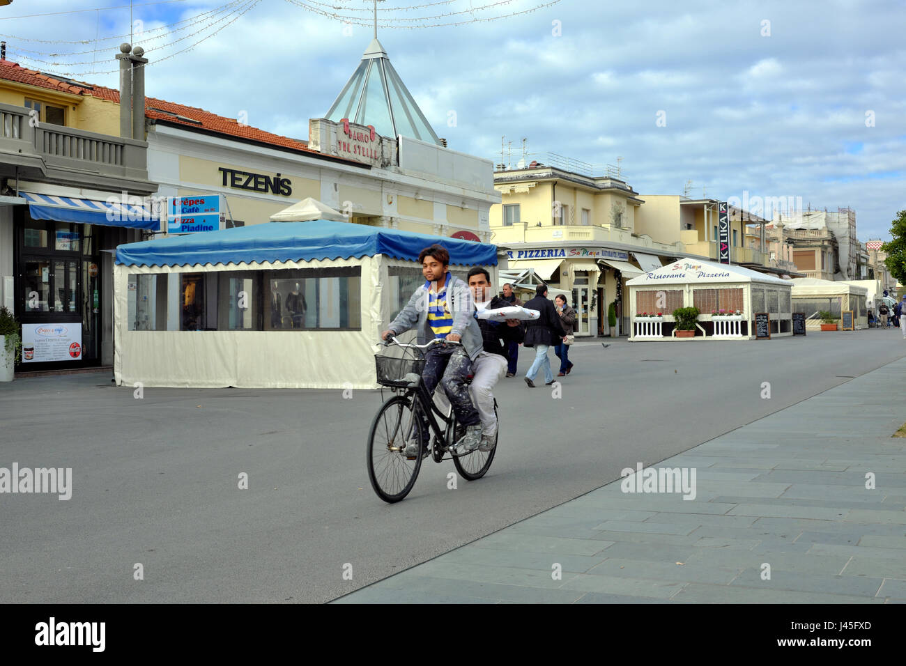 Zur Mittagszeit nachhaltigen Verkehrs - zwei männliche asiatische Arbeiter mit Mittagessen auf einer Fahrrad - Viareggio Promenade, Toskana, Italien, Europa Stockfoto