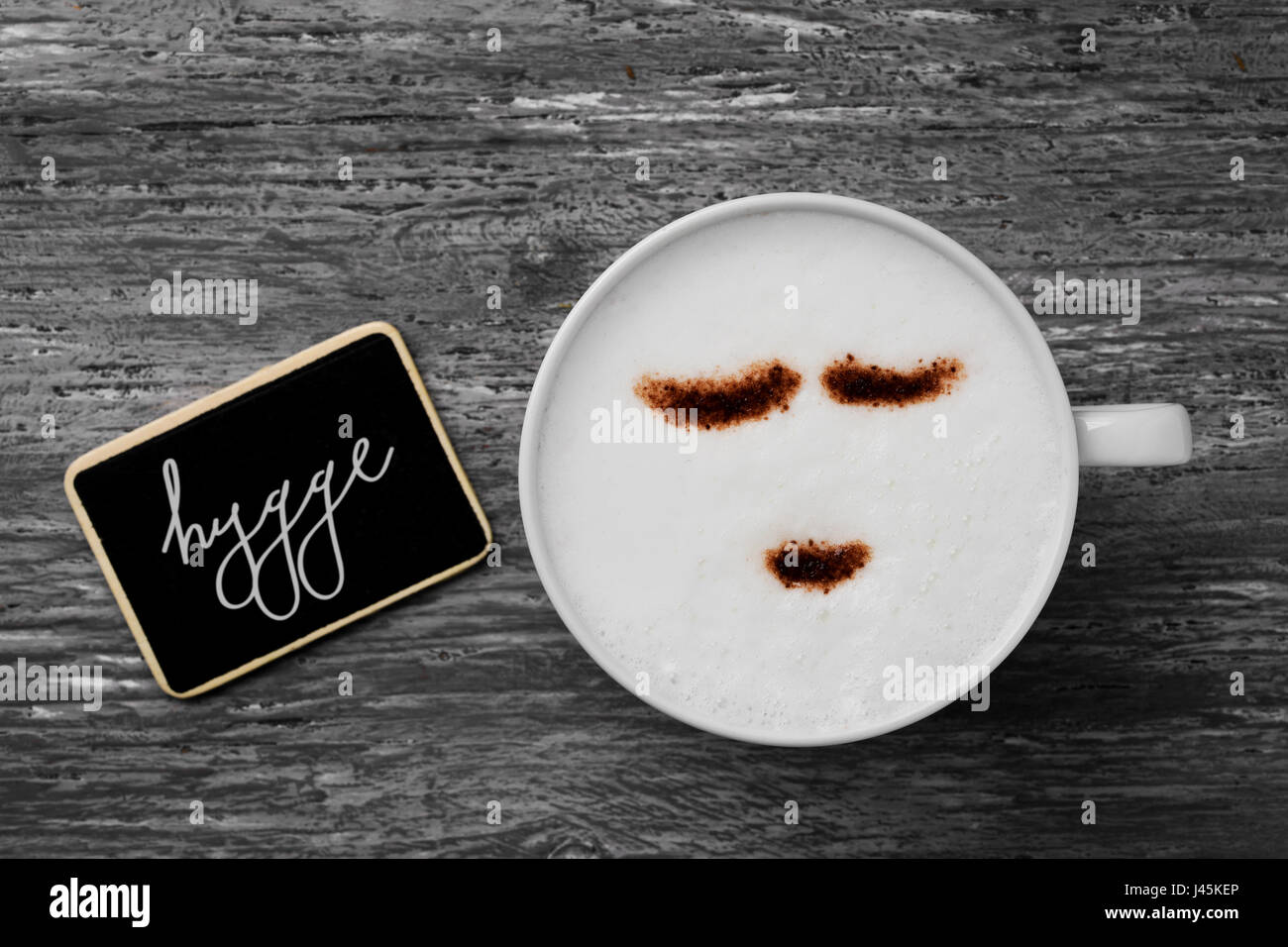 High-Angle Shot von einer Tasse Cappuccino mit ein glückliches Gesicht gezeichnet mit Kakaopulver und ein Schild mit dem Text Hygge, dänischen und norwegischen Wort für Stockfoto