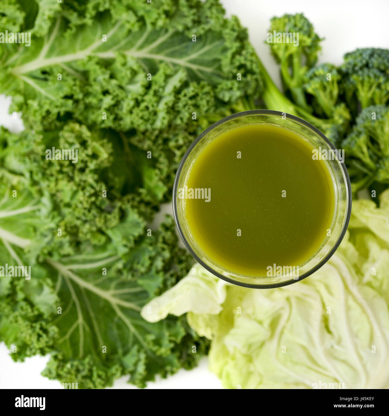 High-Angle Shot eine Grünkohl-Smoothie serviert in einem Glas und einige Blätter von Kale auf weißem Hintergrund Stockfoto