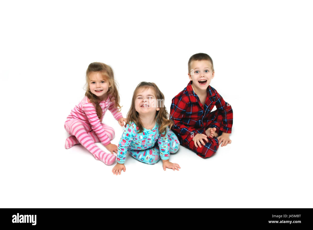 Drei Kinder reagieren mit Begeisterung am Weihnachtsmorgen.  Jeder hat eine andere Reaktion auf ihren Gesichtern.  Es gibt drei; ein Junge und zwei Mädchen. Stockfoto