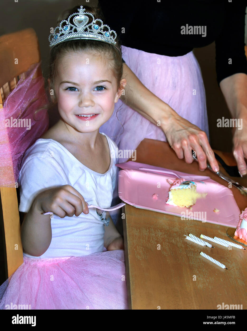 Wunderschönes kleines Mädchen genießt ihre Ballerina-Geburtstags-Party.  Sie trägt eine Krone und rosa Tutu.  Ihre Gabel ist bereit, ihre Scheibe c Essen bereit. Stockfoto