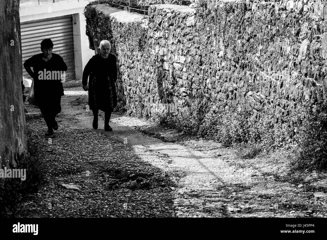 Piqeras, Albanien. 1. Mai 2017. Witwen in schwarz gehen Sie eine Gasse in Piqeras. Balkan Witwen des Krieges werden voraussichtlich in ewiger Trauer um ihren verstorbenen Mann unverheiratet bleiben. Albanien hat eine Bevölkerung von knapp über 3 Millionen, nur ein Drittel der alle Albaner in der Welt aufgrund der negativen Migration. Fast 60 % der Bevölkerung sind Muslime, in der Nähe von 20 % arbeitslos und 15 % unterhalb der Armutsgrenze. Der Übergang vom Kommunismus, die in den 1990er Jahren begann hat bewiesen Herausforderung aufgrund der hohen Arbeitslosigkeit, weitverbreitete Korruption, marode Infrastruktur und leistungsstarke organisiertes Verbrechernetze. Die Länder Stockfoto