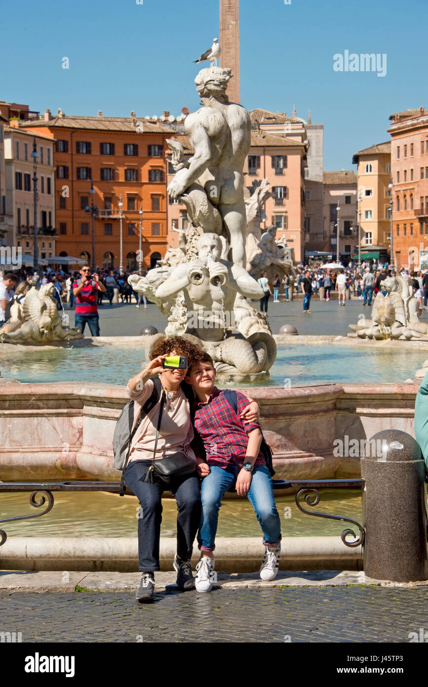 Fontana del Moro oder Moor-Brunnen auf der Piazza Navona (Rom) mit 2 Personen Touristen Besucher mit dem Selfie Fotografieren an einem sonnigen Tag mit blauem Himmel. Stockfoto