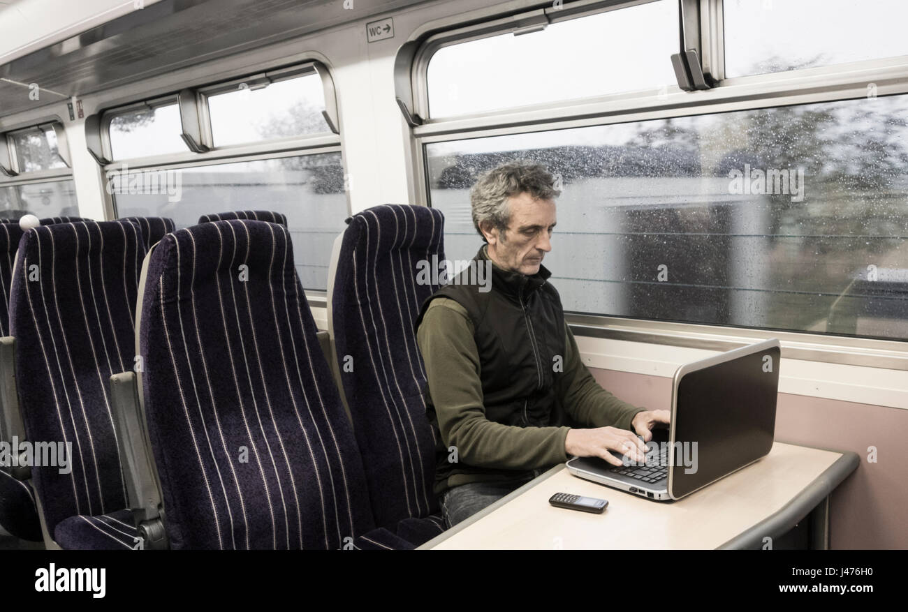 Zug UK. Reifer Mann mit Laptop am Fenster Sitz auf leere Northern Line Zug mit Regen am Fenster. England. Vereinigtes Königreich Stockfoto