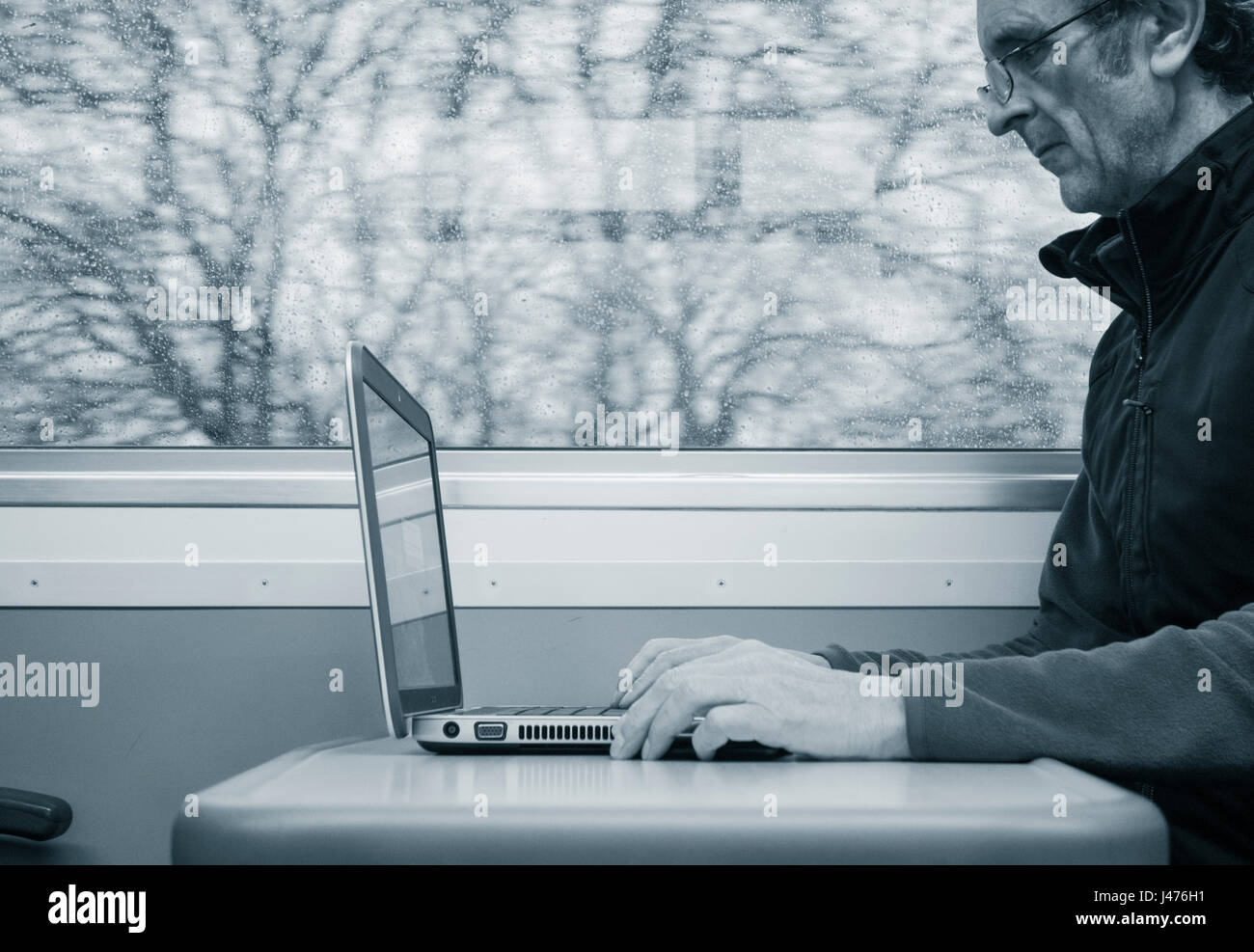 UK zu trainieren. Reifer Mann mit Laptop am Fensterplatz auf leeren Zug mit Regen am Fenster. England. Vereinigtes Königreich Stockfoto