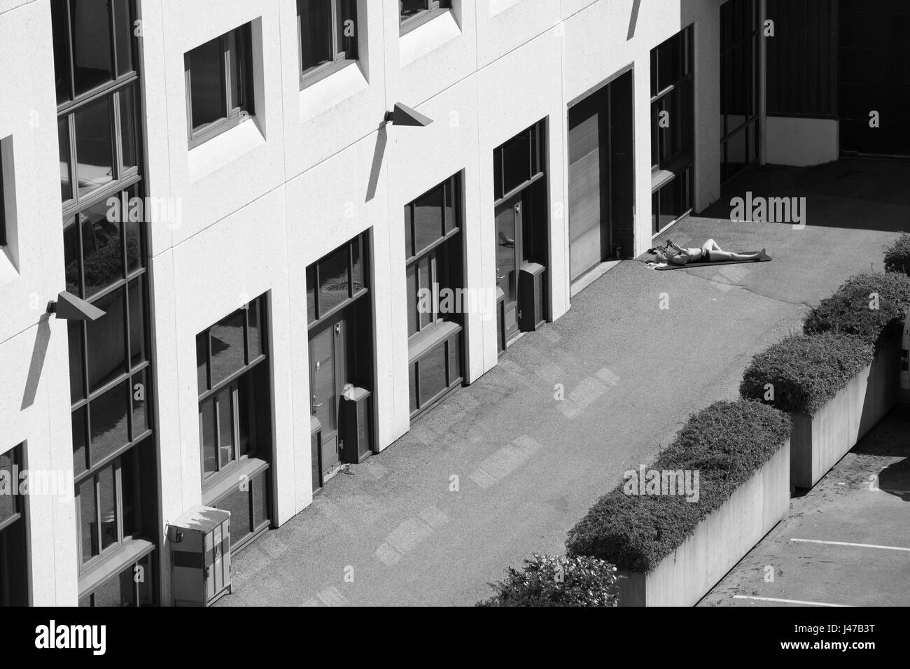 Einen Überblick über eine eine Frau Sonnenbaden außerhalb ein Bürohaus und neben einem Parkplatz in der Stadt Bergen in Norwegen Stockfoto