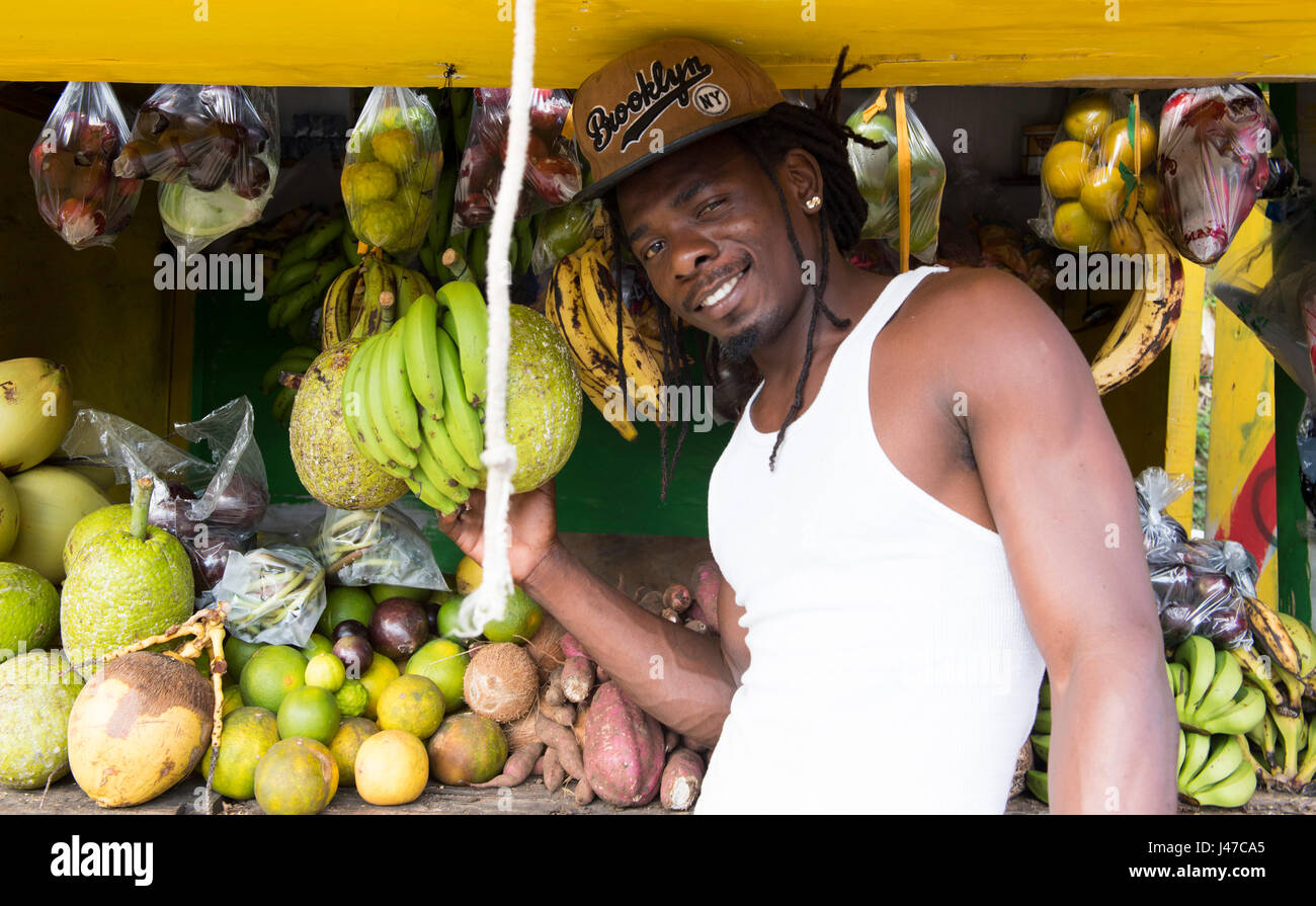 Ein Mann trägt einen amerikanischen Baseball-Cap mit Obst auf einem Stand am Straßenrand in Grenada, West Indies, Karibik Stockfoto