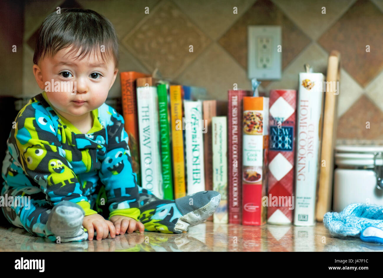 Niedlich und Happy Baby Boy tragen bunte Schlafanzug in Küche vor viele Kochbücher sitzt Stockfoto