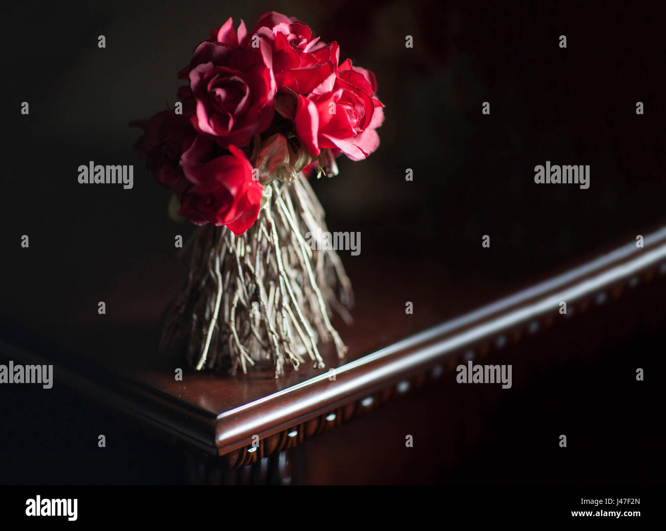 Bouquet von getrockneten roten Rosen mit verdrehten Stämmen in einem Bouquet in dunklen dramatische Beleuchtung auf einem polierten dunklem Hartholz Tisch Stockfoto