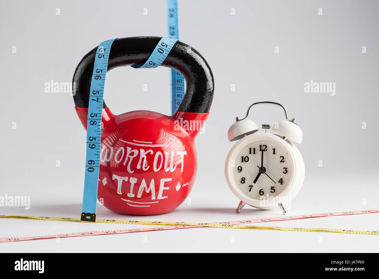 Roten Kettlebell mit Trainingszeit Schriftzüge, traditionellen Wecker und Maßband isoliert auf weiss mit Textfreiraum. Zeit um zu erarbeiten, gesunden l Stockfoto