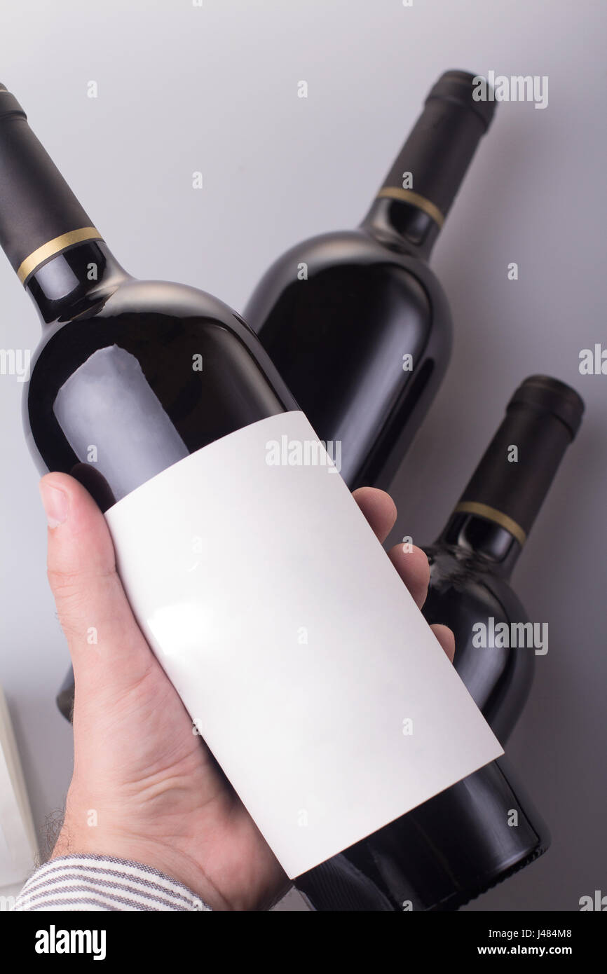 vertikale Draufsicht des kaukasischen Mann Hand hält eine Flasche Rotwein mit leere Beschriftung und zwei weitere Flasche in den Hintergrund Exemplar verfügbar Stockfoto