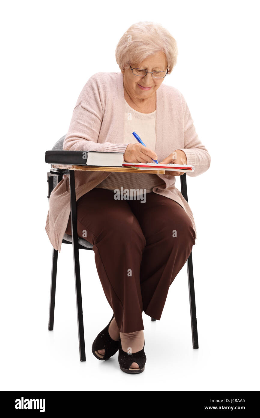 Ältere Frau in einem Schule Stuhl sitzen und schreiben isolierten auf weißen Hintergrund Stockfoto