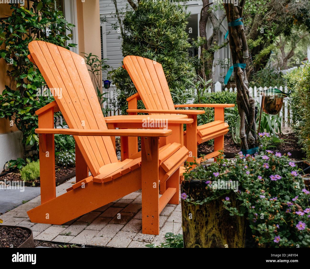 Helles orange Adirondack Liegestühle im Garten im Innenhof in Seaside, Florida USA. Stockfoto