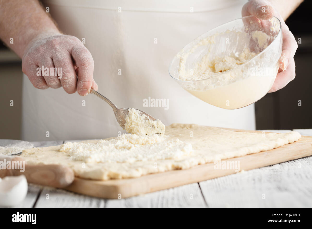 männliche Hand hob geschmolzenen Käse aus Glasschale für Käsekuchen Stockfoto