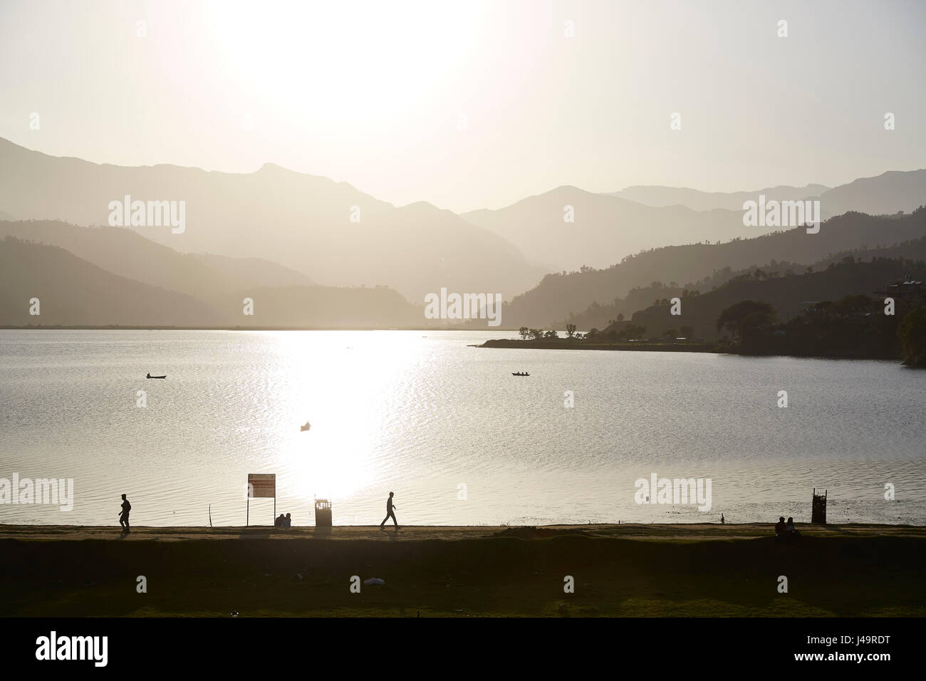 Silhouette Menschen laufen auf einem Pfad durch einen See ein See bei Sonnenuntergang, Pokhara, Nepal Stockfoto
