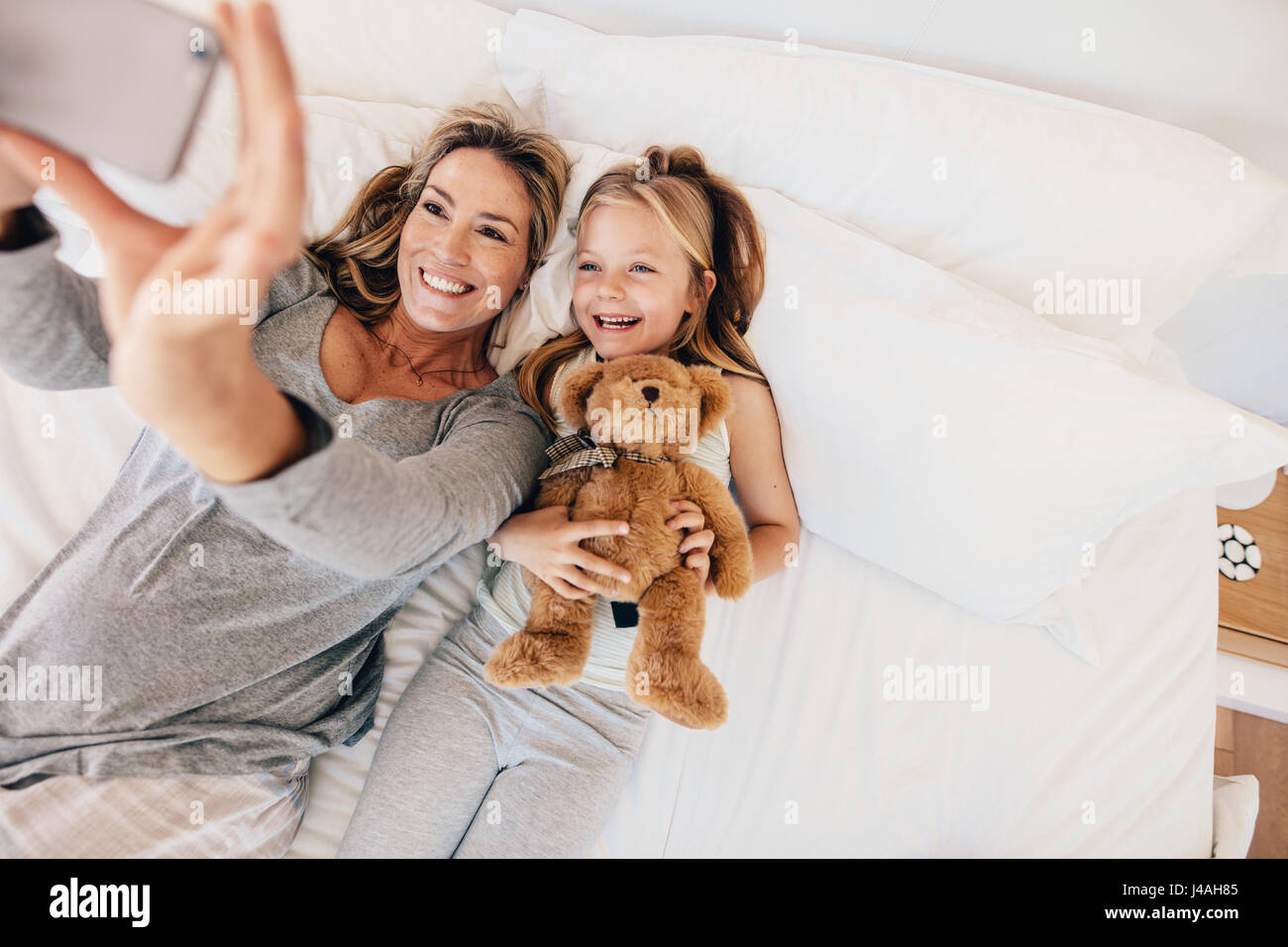 Ansicht von oben Schuss der glückliche junge Familien nehmen Selfie mit Smartphone im Bett. Mutter und Tochter am Bett nehmen Selbstporträts im Schlafzimmer liegen. Stockfoto