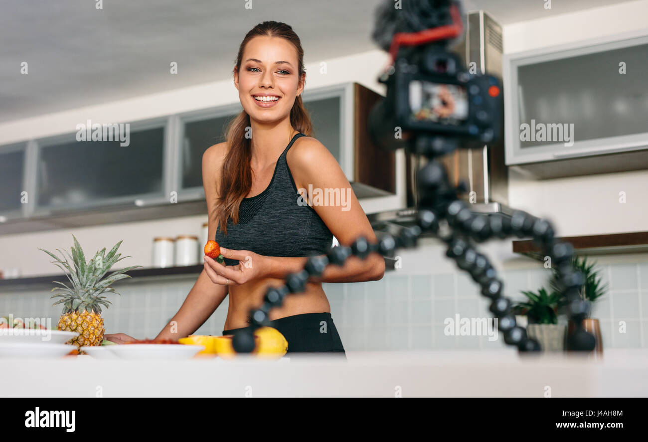 Junge Dame mit einer Erdbeere am Küchentisch, vor der Kamera. Lächelnde Frau Aufnahme Inhalt für ihr Vlog in Küche. Stockfoto