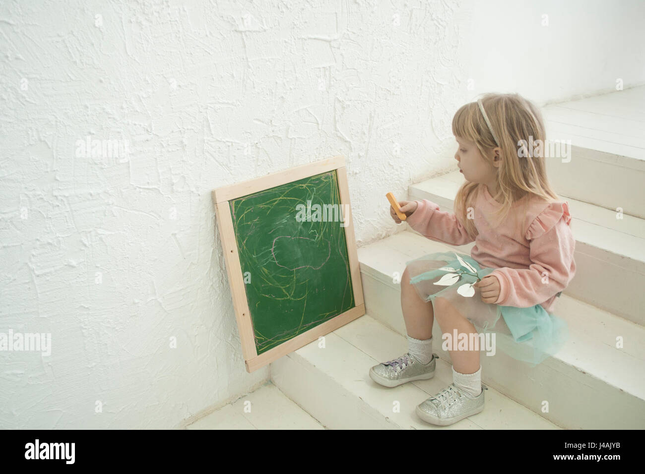 Niedlichen Kleinkind Mädchen in Silber Kopf gebunden schreiben an Kreide Tafel sitzen Stockfoto