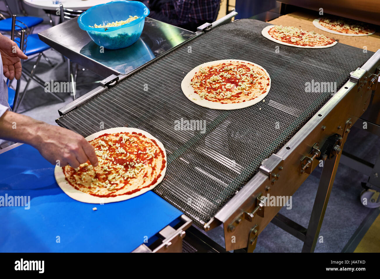 Arbeiter Koch fügt Käse auf die Pizza auf dem Förderband Stockfoto