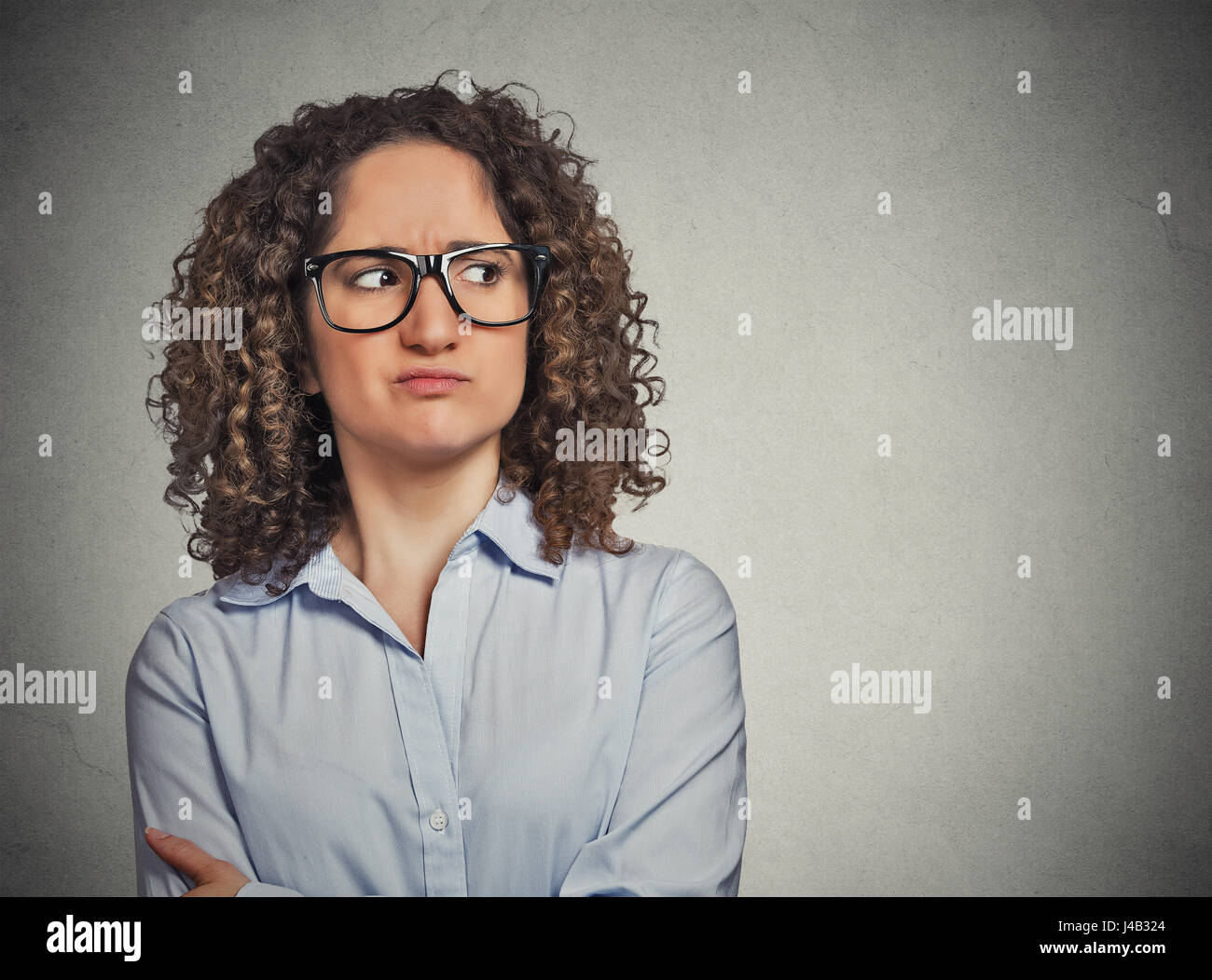 Missfallen verdächtige junge Frau mit Brille seitwärts auf grauen Hintergrund isoliert. Negative Gesichtsausdruck Emotionen Wahrnehmung Stockfoto