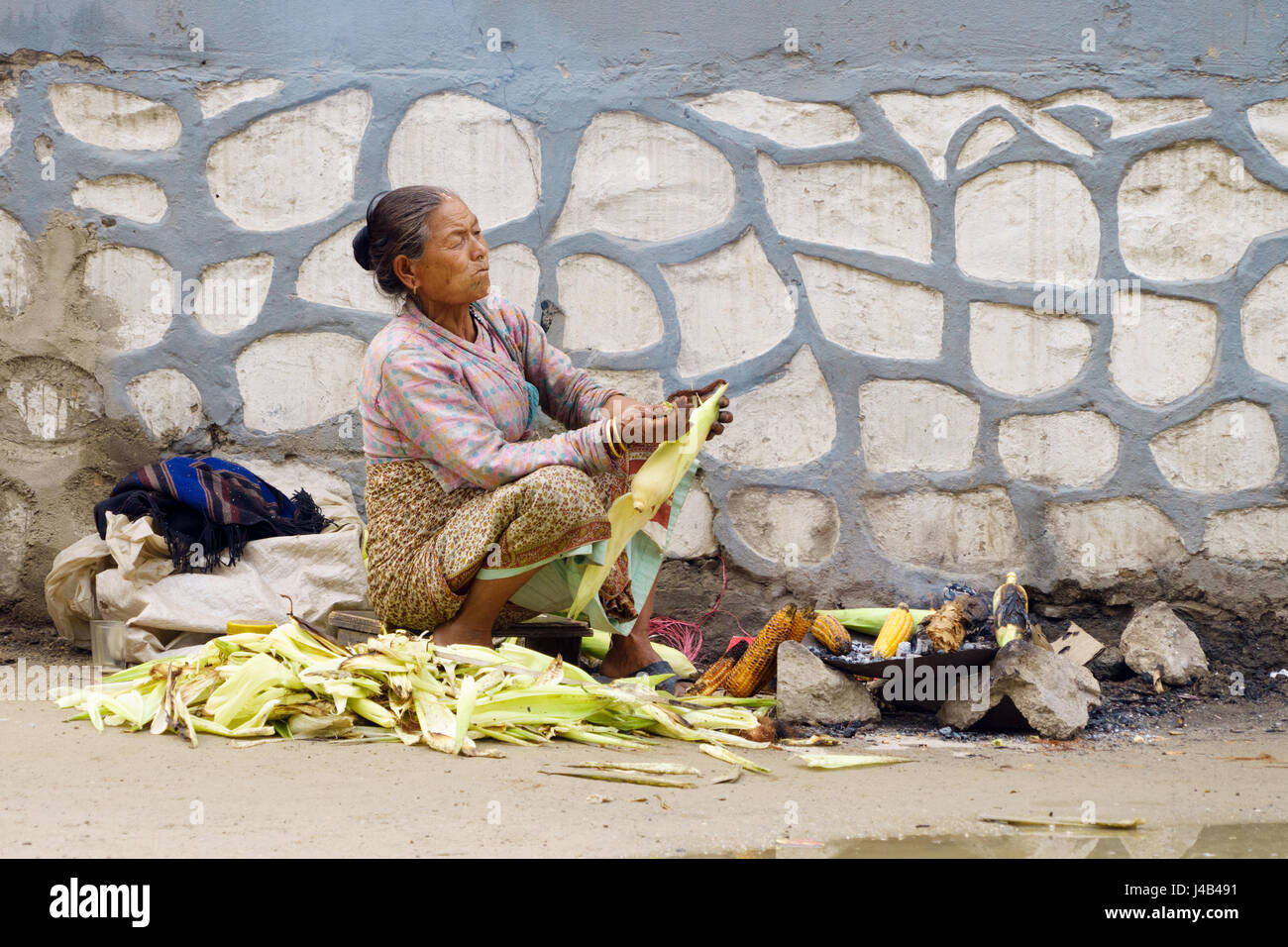 Alte bedürftige Frau rösten Mais an der Seite der Straße in stark verschmutzten Luft. Kathmandu, Nepal. Stockfoto