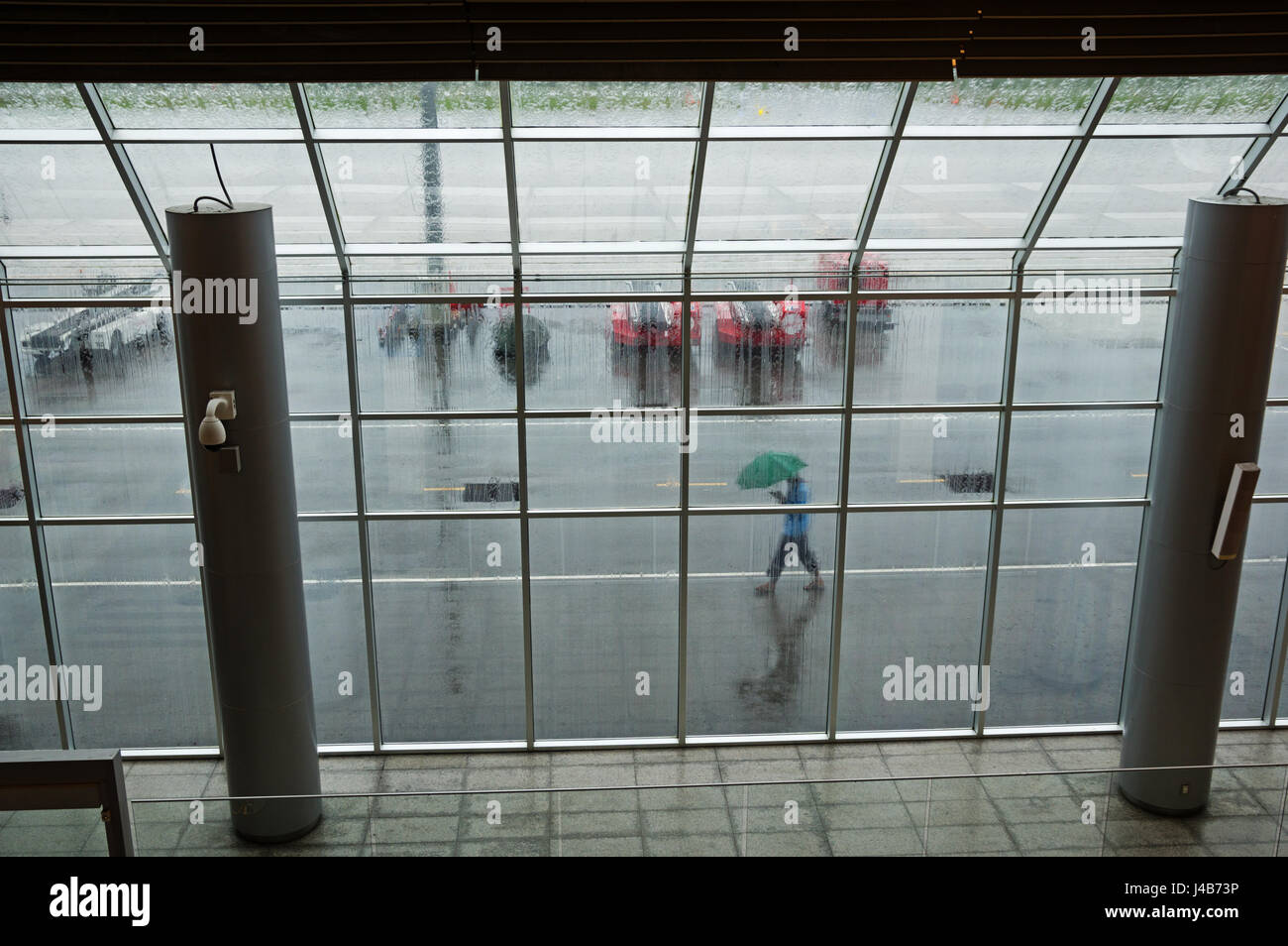 Blick durch ein Fenster der Flughafen an einem regnerischen Tag mit einer Person zu Fuß von außen mit Regenschirm Stockfoto