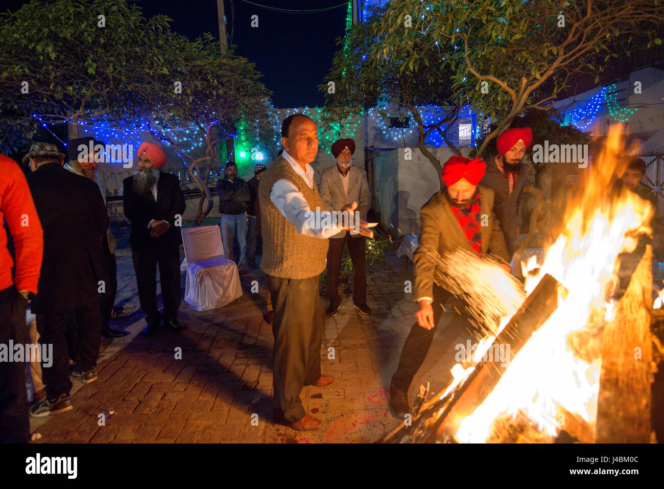 Die Männer werfen Samen in das Feuer Lohri im Punjab, Indien. Kleine Gegenstände in das Feuer werfen stellt einen Bezug auf Feuer und die Elemente. Stockfoto