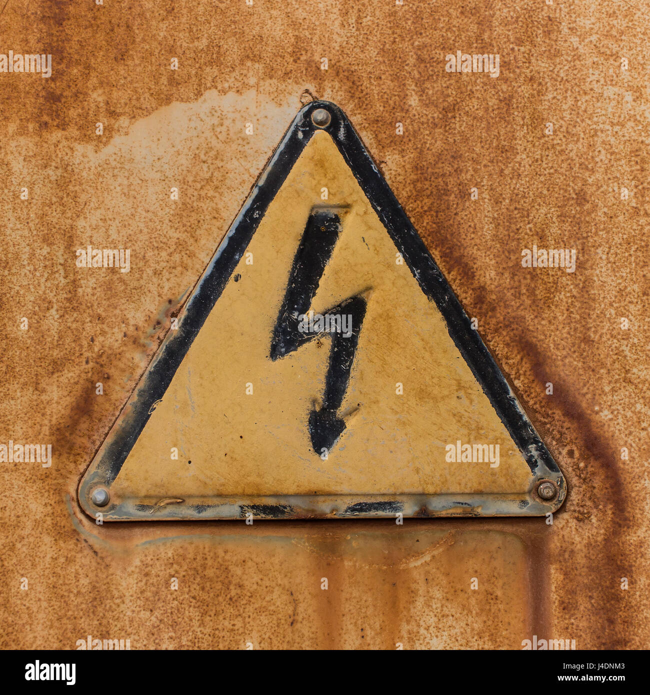Alten dreieckigen Hochspannung Zeichen auf ein Blatt von rostigen Eisen durch Nieten befestigt. Stockfoto