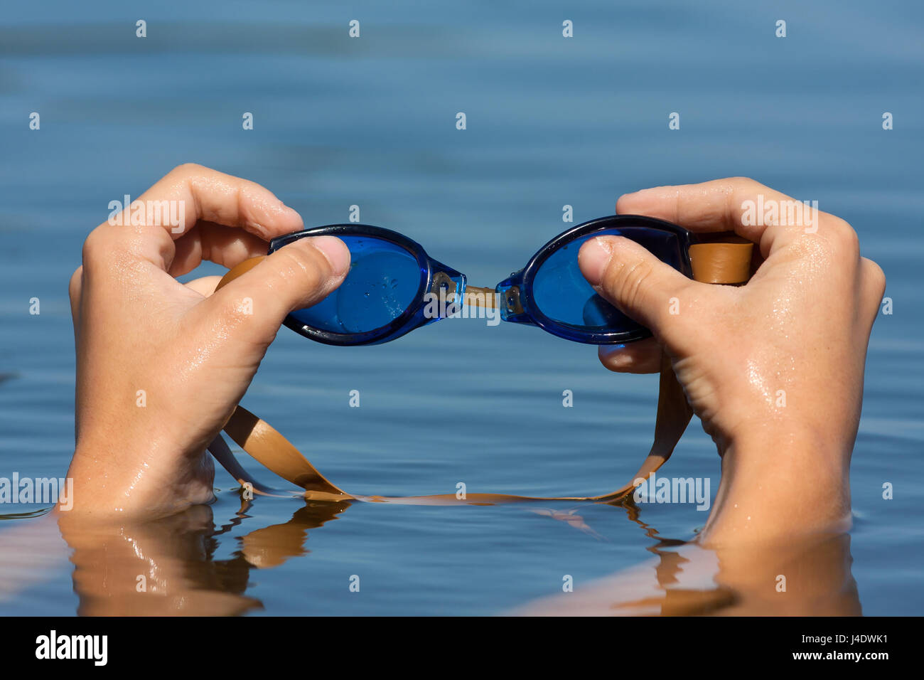 Hand der Schwimmer holding Schwimmbrille auf blauem Wasser Hintergrund Stockfoto