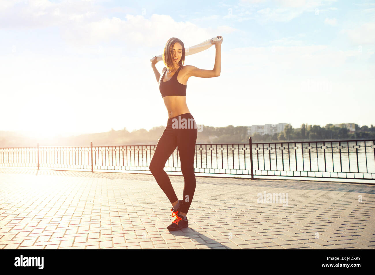 Lächelnde Jogger Frau am See bei Sonnenuntergang. Sport- und Lifestyle-Konzept Stockfoto