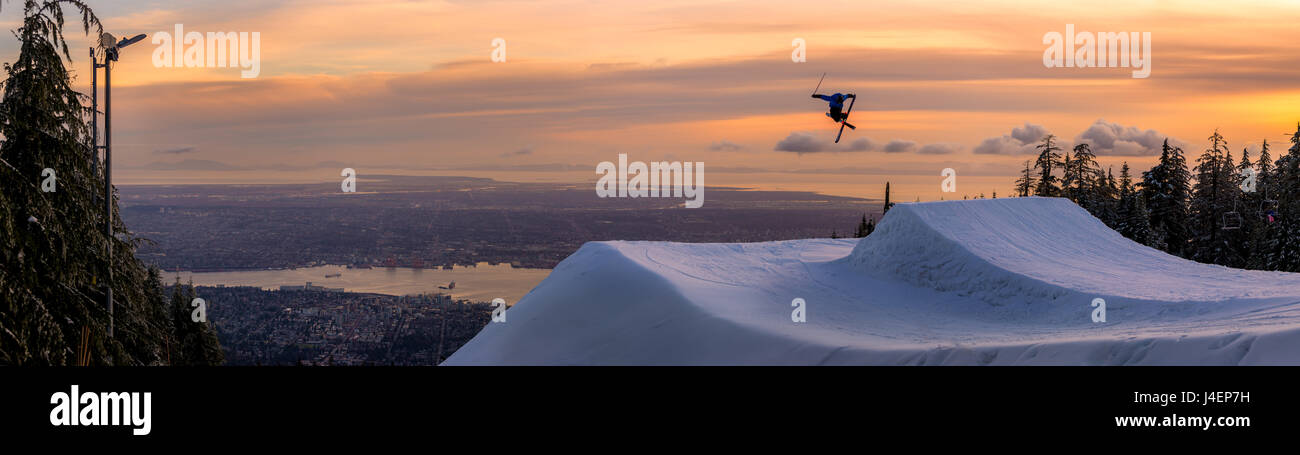 Freestyle-Skifahrer machen einen Trick aus einem Sprung über die Stadt bei Sonnenuntergang, Kanada, Nordamerika Stockfoto