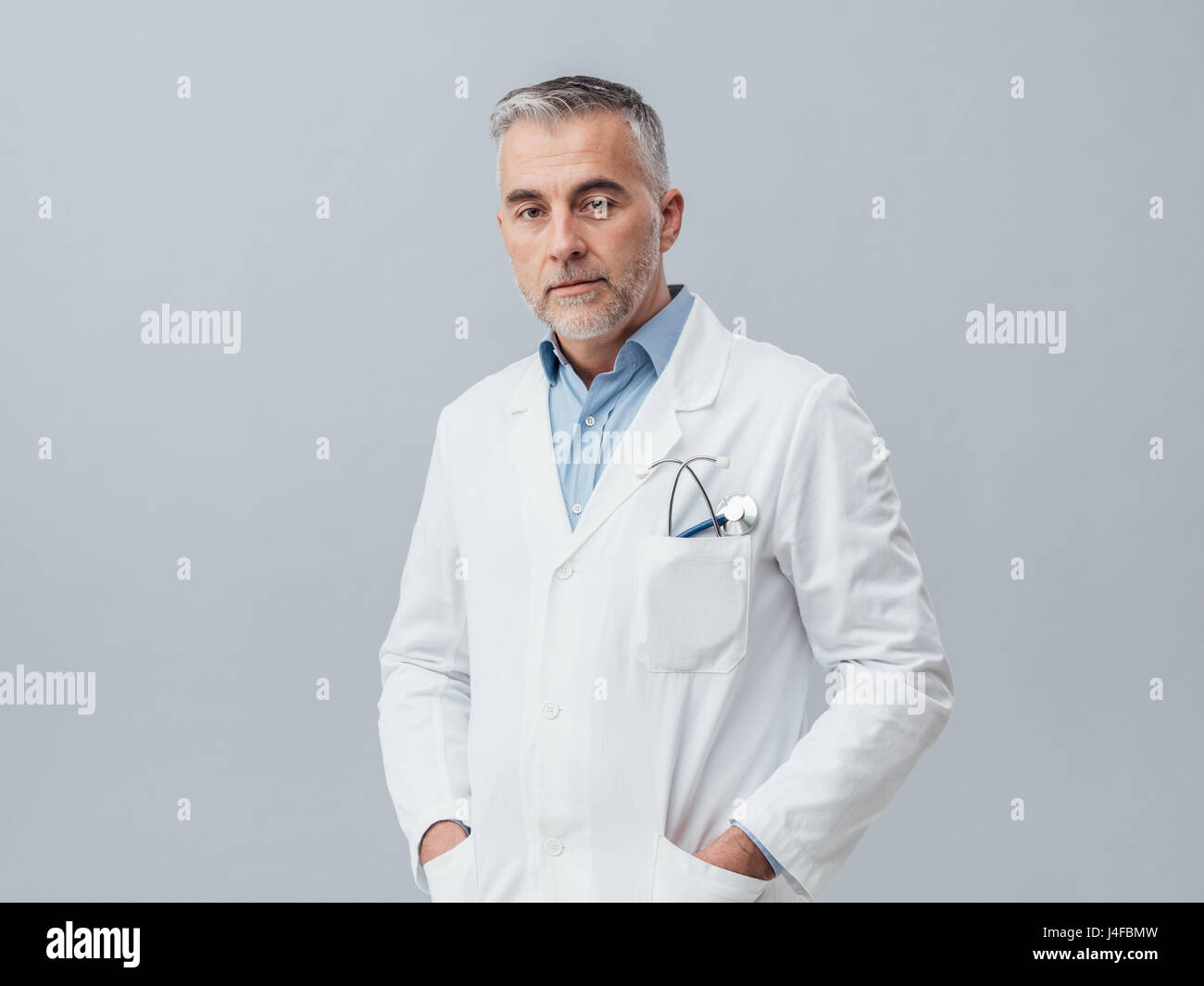 Zuversichtlich Arzt trägt einen Laborkittel und posiert, er schaut in die Kamera Stockfoto