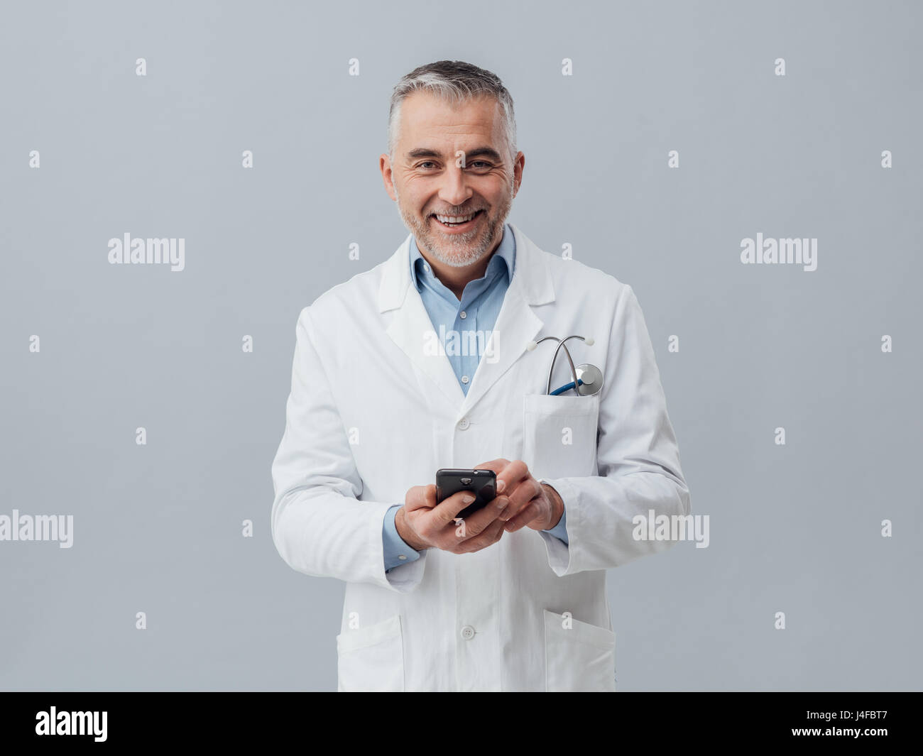 Lächelnde Reife Arzt mit seinem Smartphone zu verbinden und dabei eine medizinische Beratung online Stockfoto