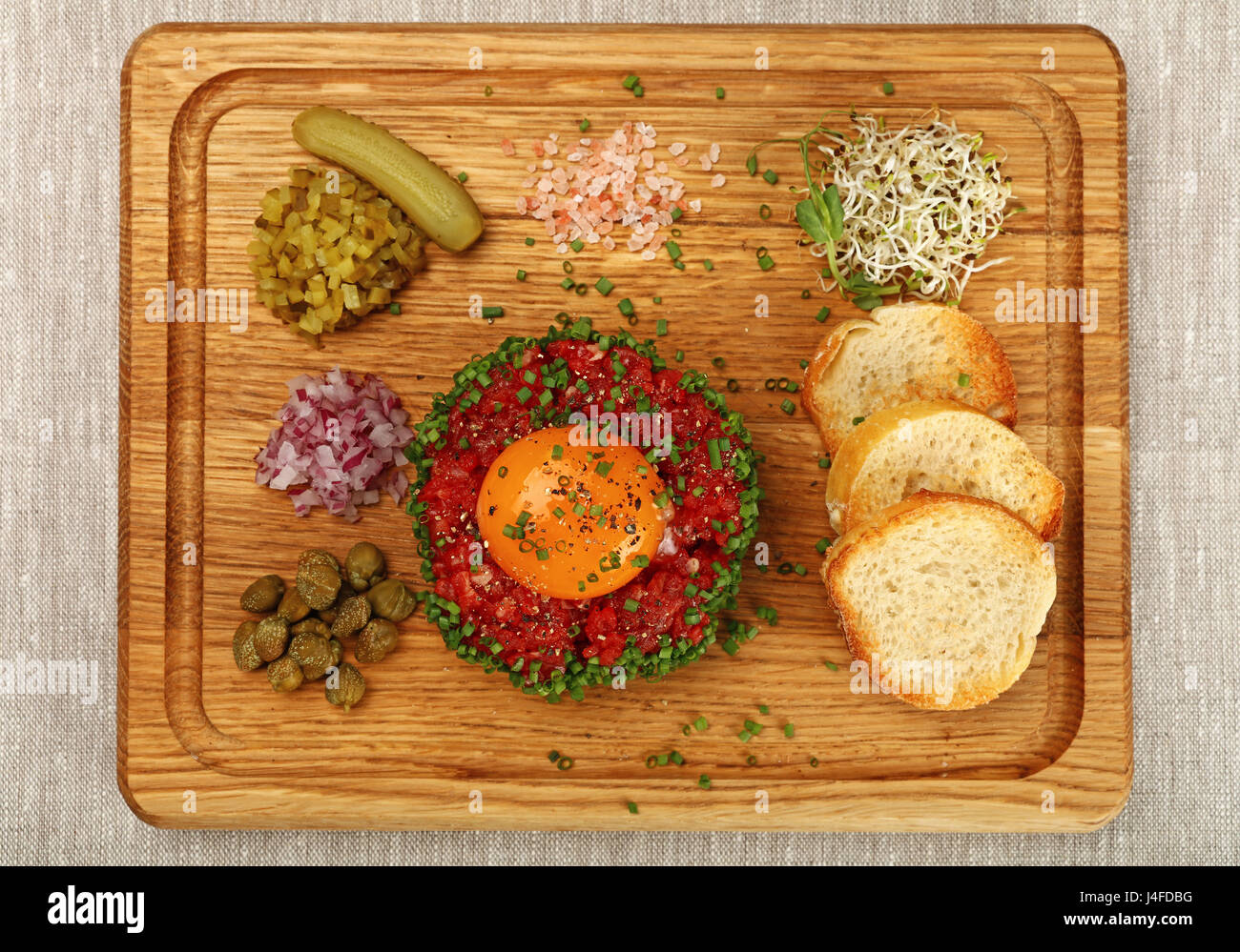 Eine Portion rohes Hackfleisch Fleisch Tartar Steak mit Eigelb, Zwiebeln, Gurken, Kapern, Salz und Toast serviert am Holzbrett, Nahaufnahme, erhöhte Stockfoto