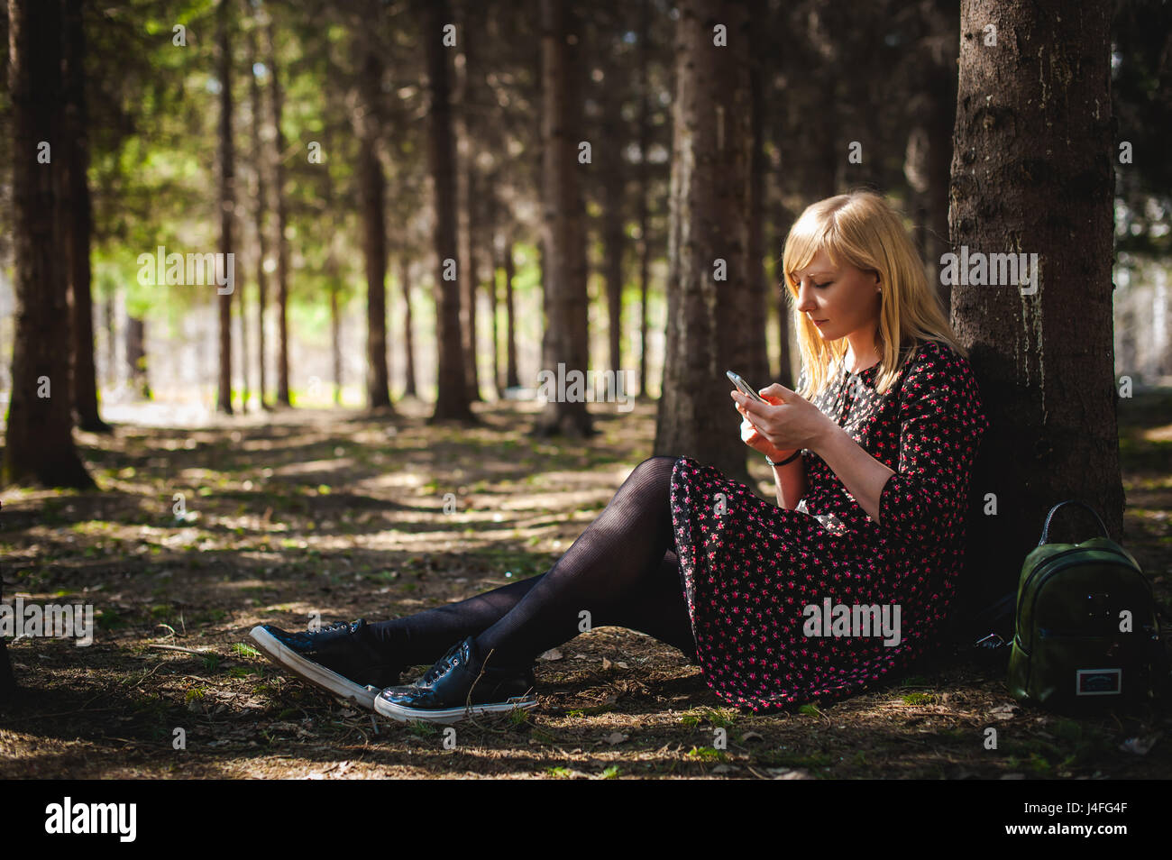 blonde Frau gekleidet Sommerkleid, schwarzer Strumpfhose und Turnschuhe mit  weißer Sohle, Natur genießen der warmen, sonnigen Tag ruhen. Sitzt unter  Baum allein, holdin Stockfotografie - Alamy