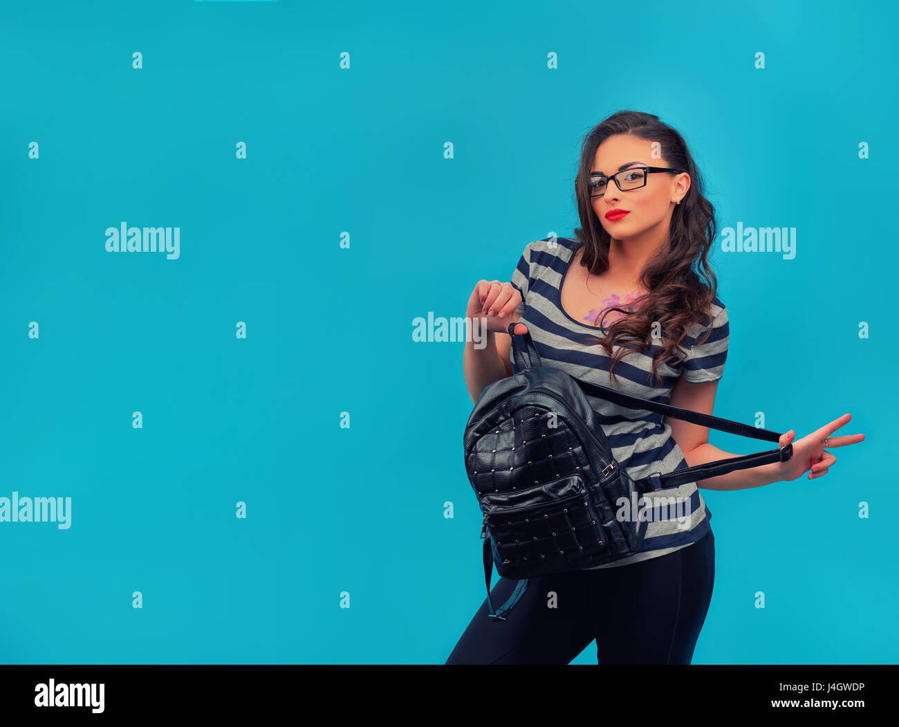 Stilvolle junge Mädchen mit einem Rucksack aus Leder in einem gestreiften Vintage Shirt mit Tattoo auf dem blauen Hintergrund. Junge weibliche Modell. Stockfoto