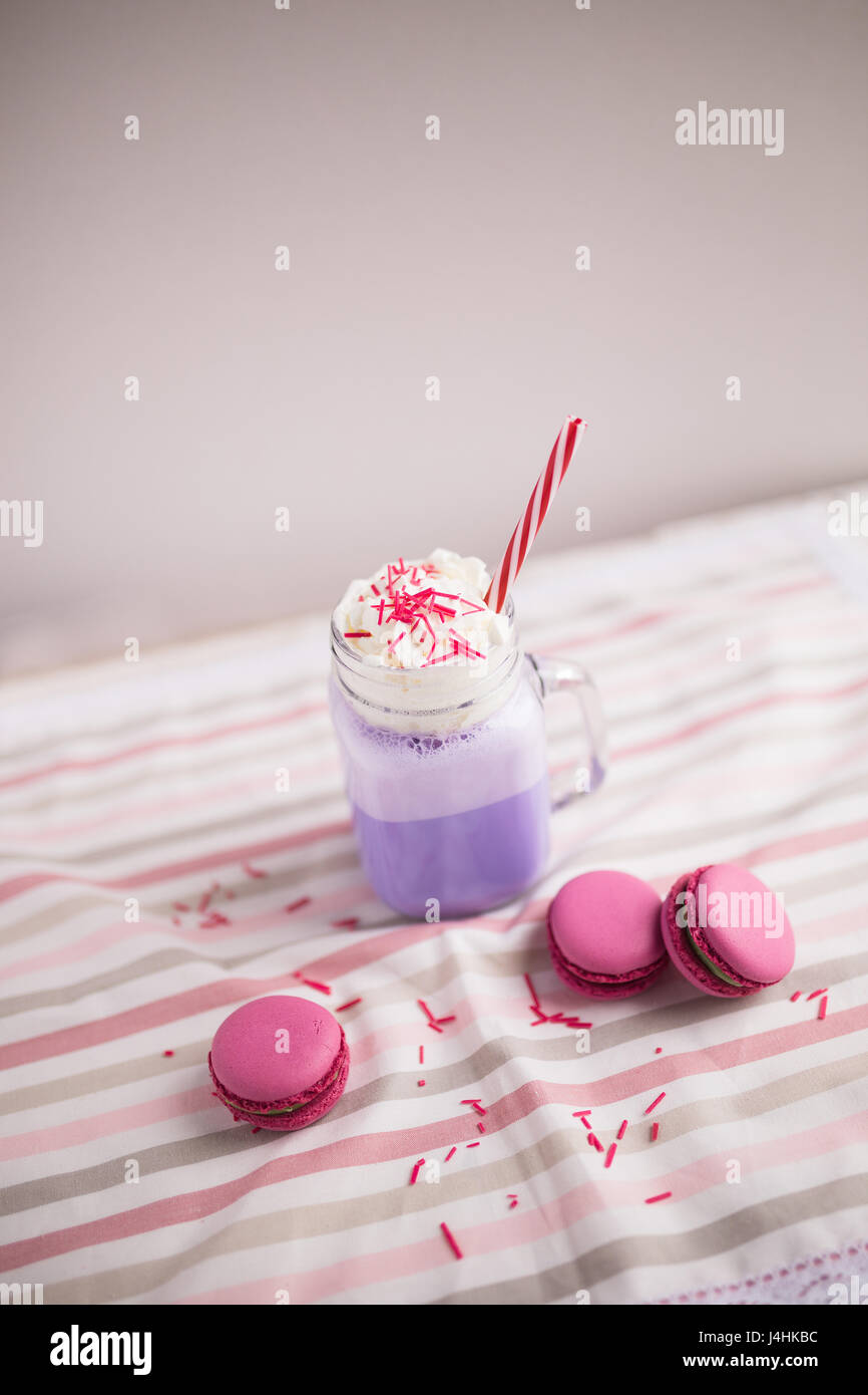 Lila Kaffee in Tasse stilisierte Einmachglas mit Macarons und Rosen und bunte Dekoration. Heidelbeer-Milch-Shake. Einhorn-Kaffee. Einhorngericht Stockfoto