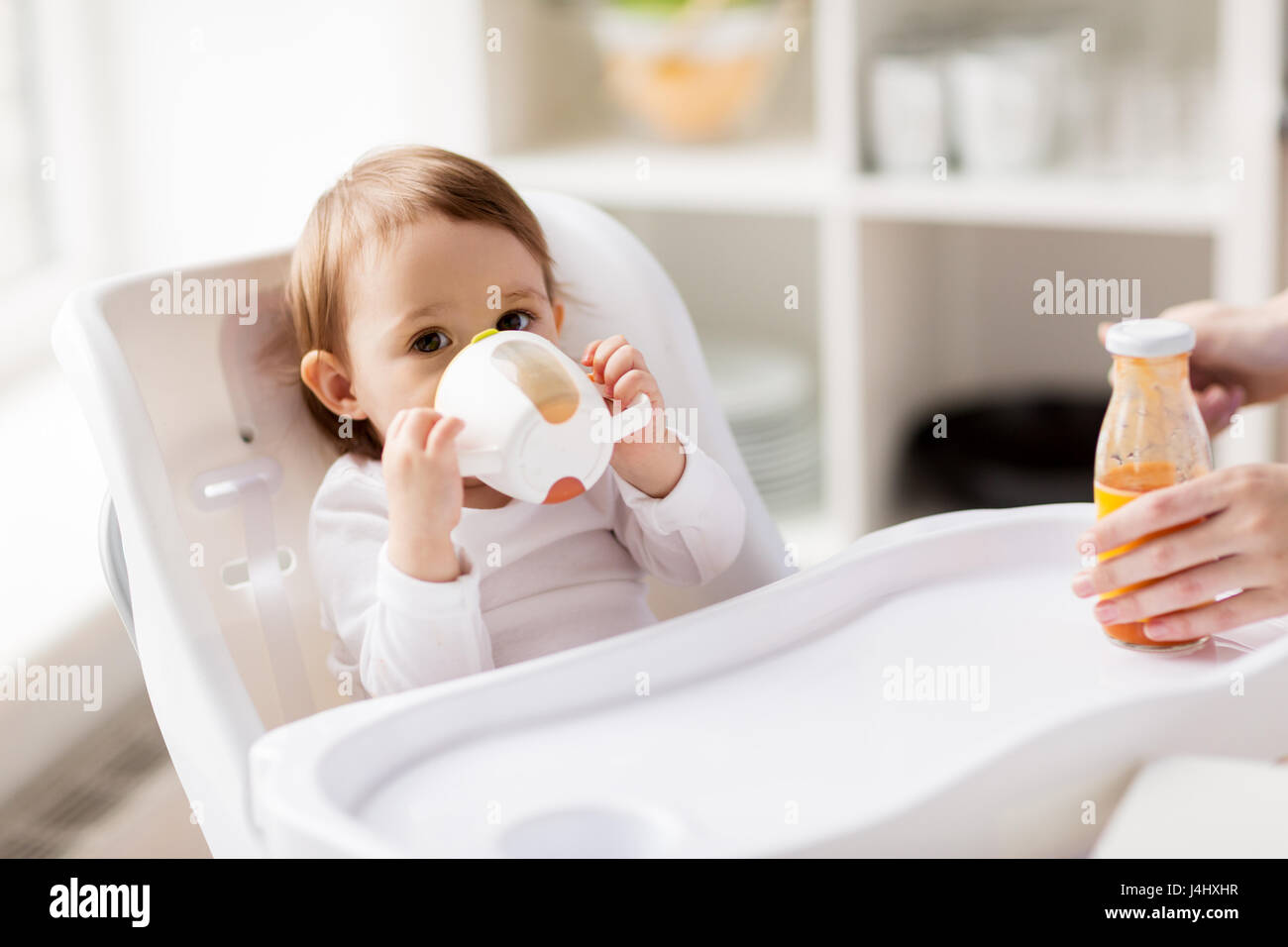 Baby trinken aus Auslauf Tasse im Hochstuhl zu Hause Stockfoto