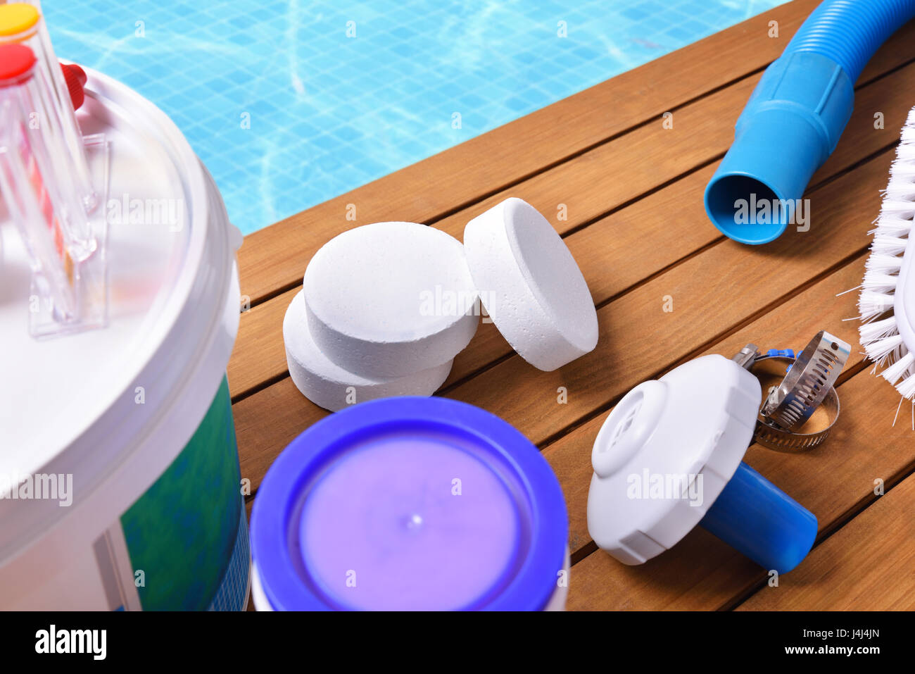 Chemische Produkte und Werkzeuge für die Wartung des Pools auf Holzlatten. Pool mit Wasser und blauen Mosaiken Hintergrund. Horizontale Komposition. Nach oben Stockfoto